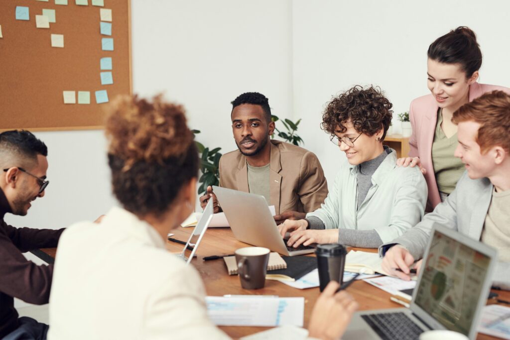 A group of professionals in an office sitting around a table with laptops, papers, and coffee cups on the table.